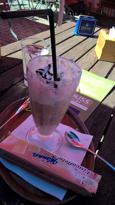 A tall glass of Eiskaffee on a table in the shade, other end of table is in bright sunlight