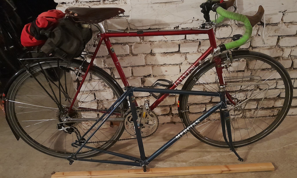 red Alves bicycle leaning against a wall. In fronto of it a smaller, blue Mercian frame rests on the floor