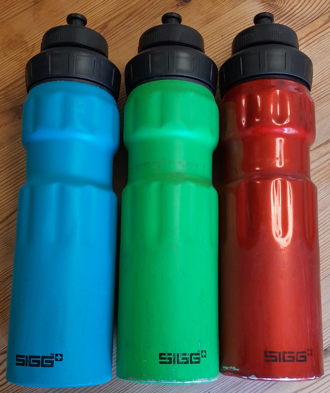 Three aluminium bike bottles: one matt blue, one matt green and one with a translucent red finish. They are 750 ml, which means they have a narrow section about 2/3 of the way up, for the cage to grip.