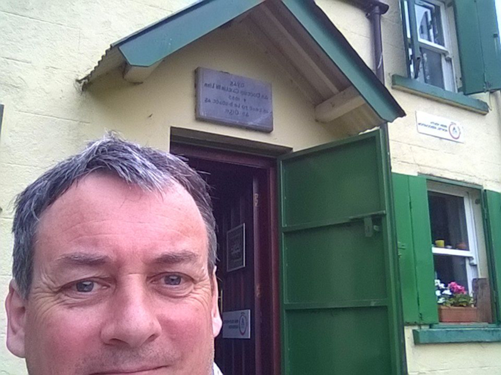 A man's face in front of a cream-coloured house with a green door