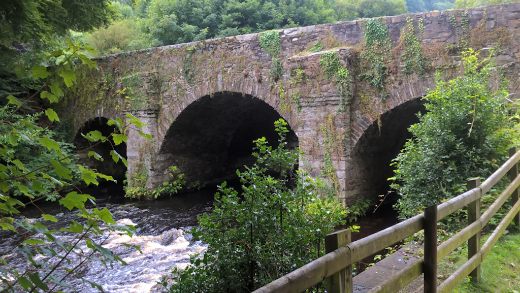 A substantial stone arched bridge over a river, among green trees
