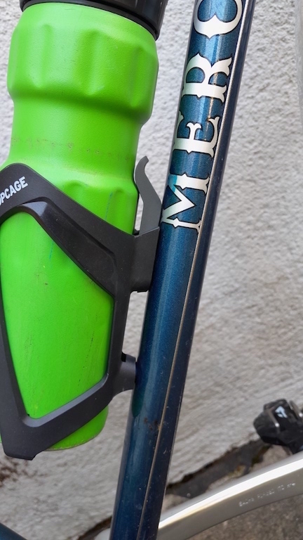 Close up of a green bottle sitting in the SKS Topcage, from the side, showing how the tab at the top snugly holds the waist of the bottle.